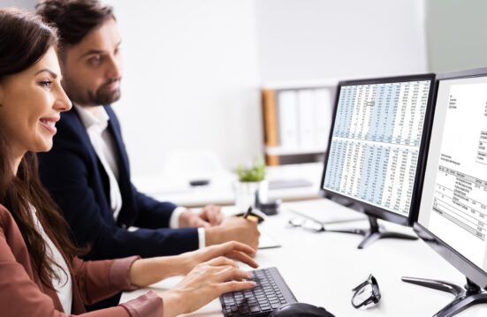 Deux professionnels travaillent au bureau devant deux écrans affichant un tableau de données financières et une facture électronique