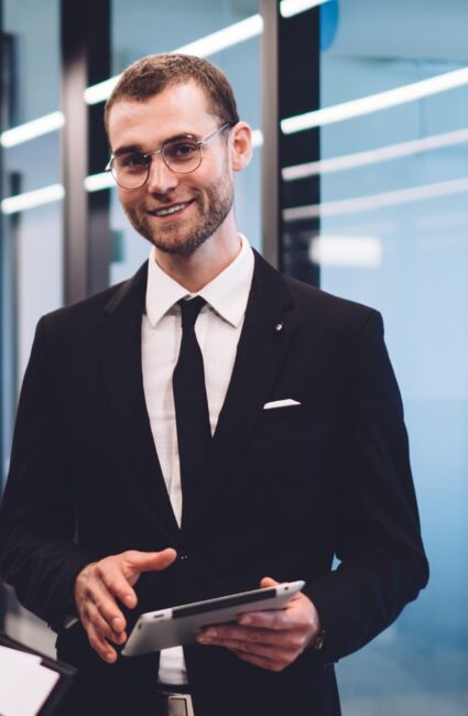 Un consultant en costume tient une tablette dans un environnement de bureau moderne.