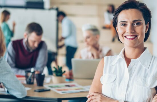 Une professionnelle souriante au premier plan dans un bureau, entourée de collègues en réunion, illustrant la gestion RH et la modernisation de la paie.
